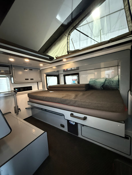 RV rental: a cozy, compact interior featuring a made bed, pop-top roof, and built-in storage/controls. Ideal for travel.