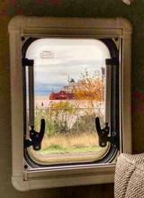 Scenic RV rental view: The red 'Presque Isle' ship on water, framed by an RV window with autumn foliage.