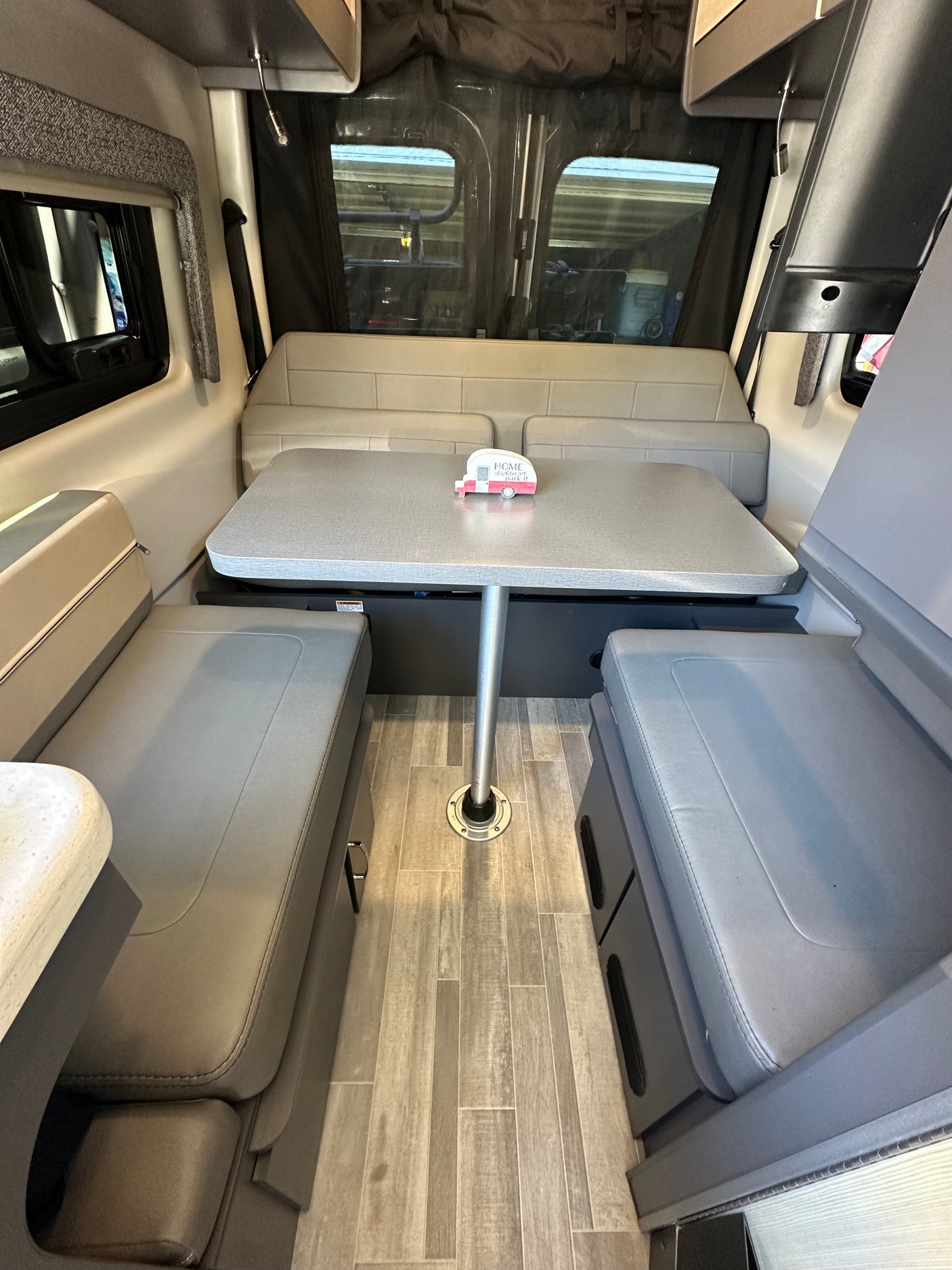 RV rental interior showing a comfortable dinette with grey benches, central table, and light wood-look floor. Great for road trips.