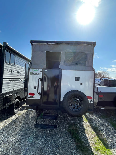 Bright sun shines on two rv rental options: a white pop-up camper next to a travel trailer, parked on a gravel lot.