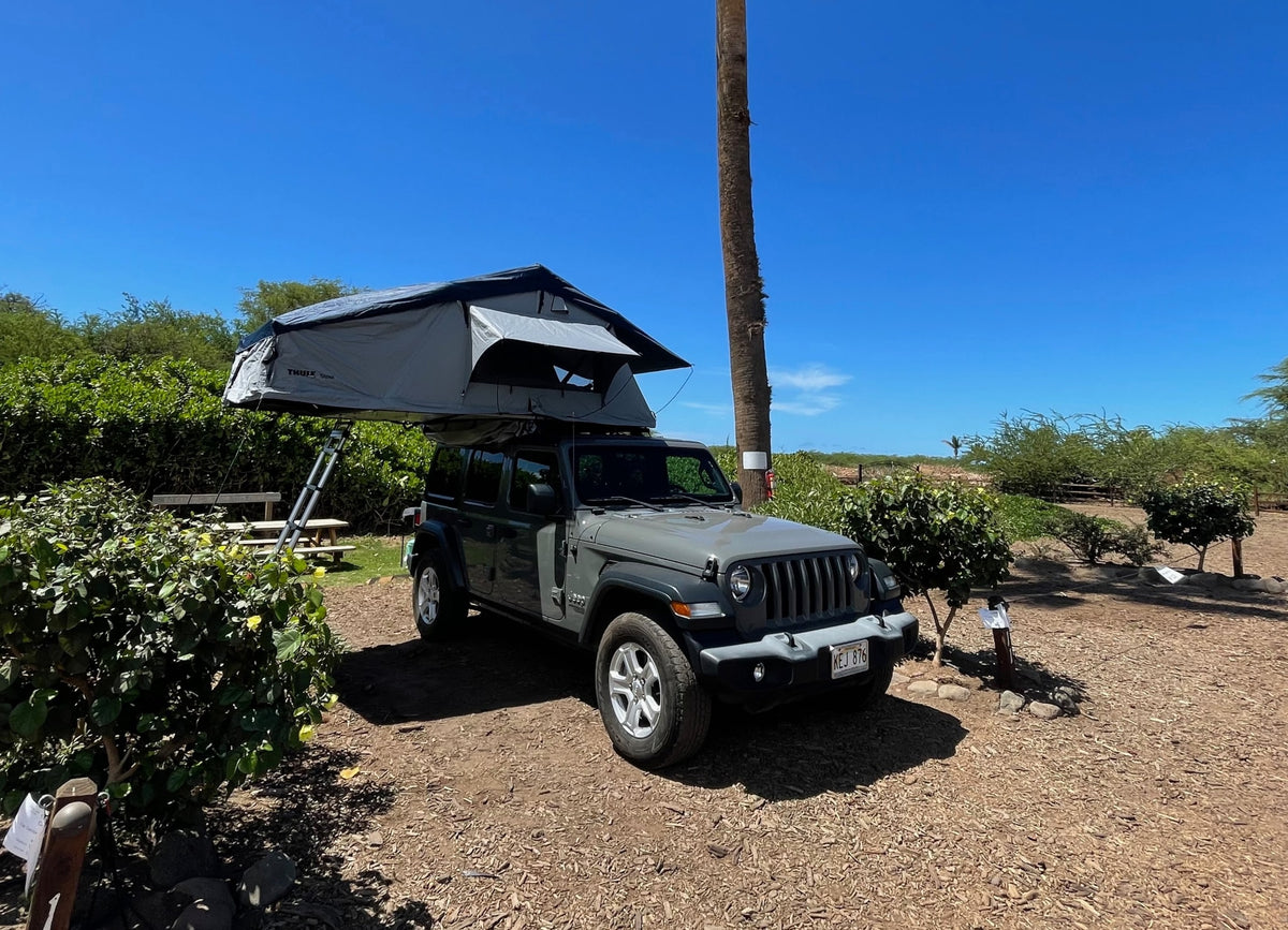 This gray Jeep Wrangler with a deployed Thule rooftop tent acts as an RV rental