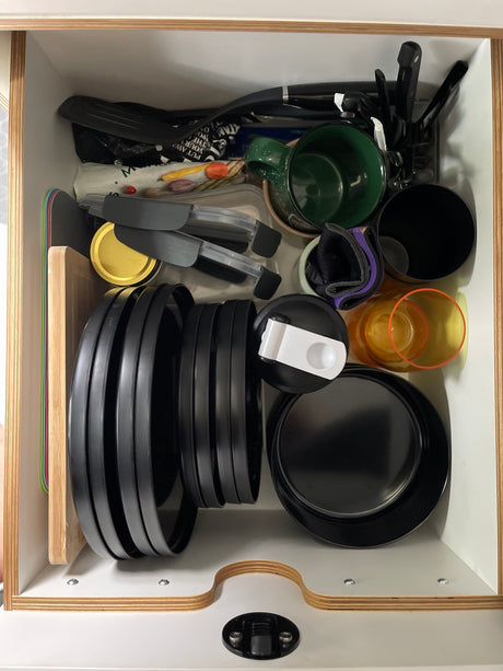 RV rental kitchen drawer neatly organized with plates, cups, cutting boards, and cooking utensils for compact storage.