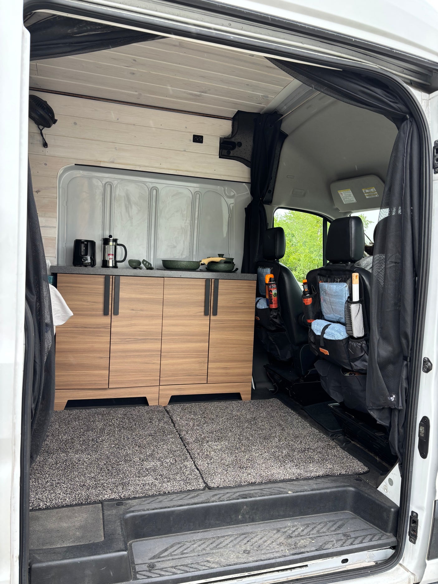 Inside this RV rental: A modern van conversion with wood cabinetry, full kitchenette, and organized front seats. Ready for travel!