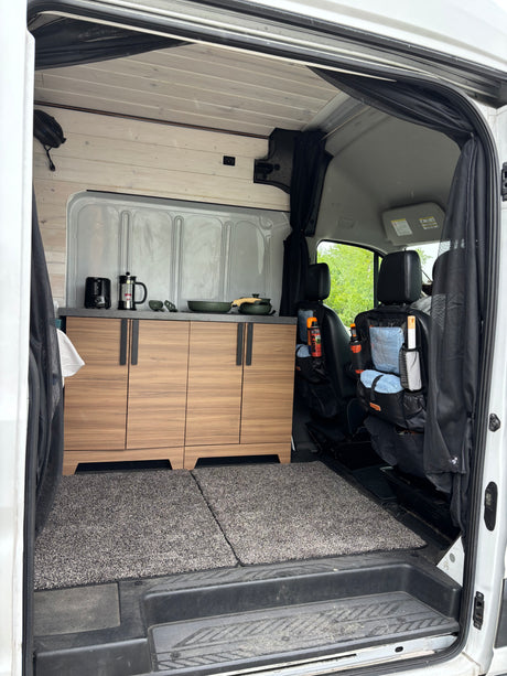 Inside this RV rental: A modern van conversion with wood cabinetry, full kitchenette, and organized front seats. Ready for travel!