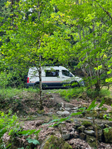 White rv rental parked in a lush green forest, blending into nature. Perfect for outdoor adventures.
