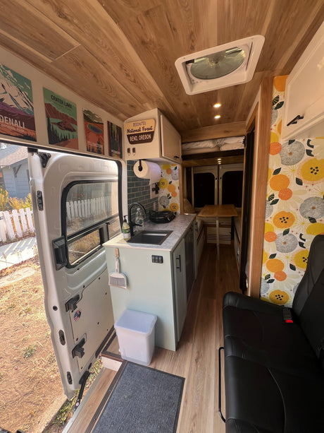 Step into this modern RV rental's camper van interior, featuring a functional kitchen, cozy living space, and wood-paneled ceiling.