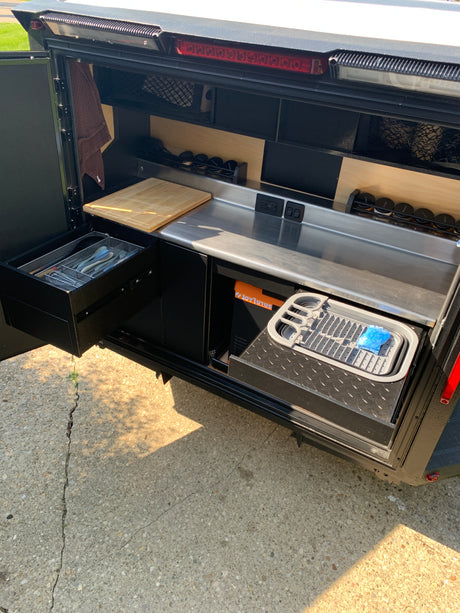 Functional outdoor kitchen setup in an RV rental, showcasing pull-out storage, stainless steel counter, and organized compartments.