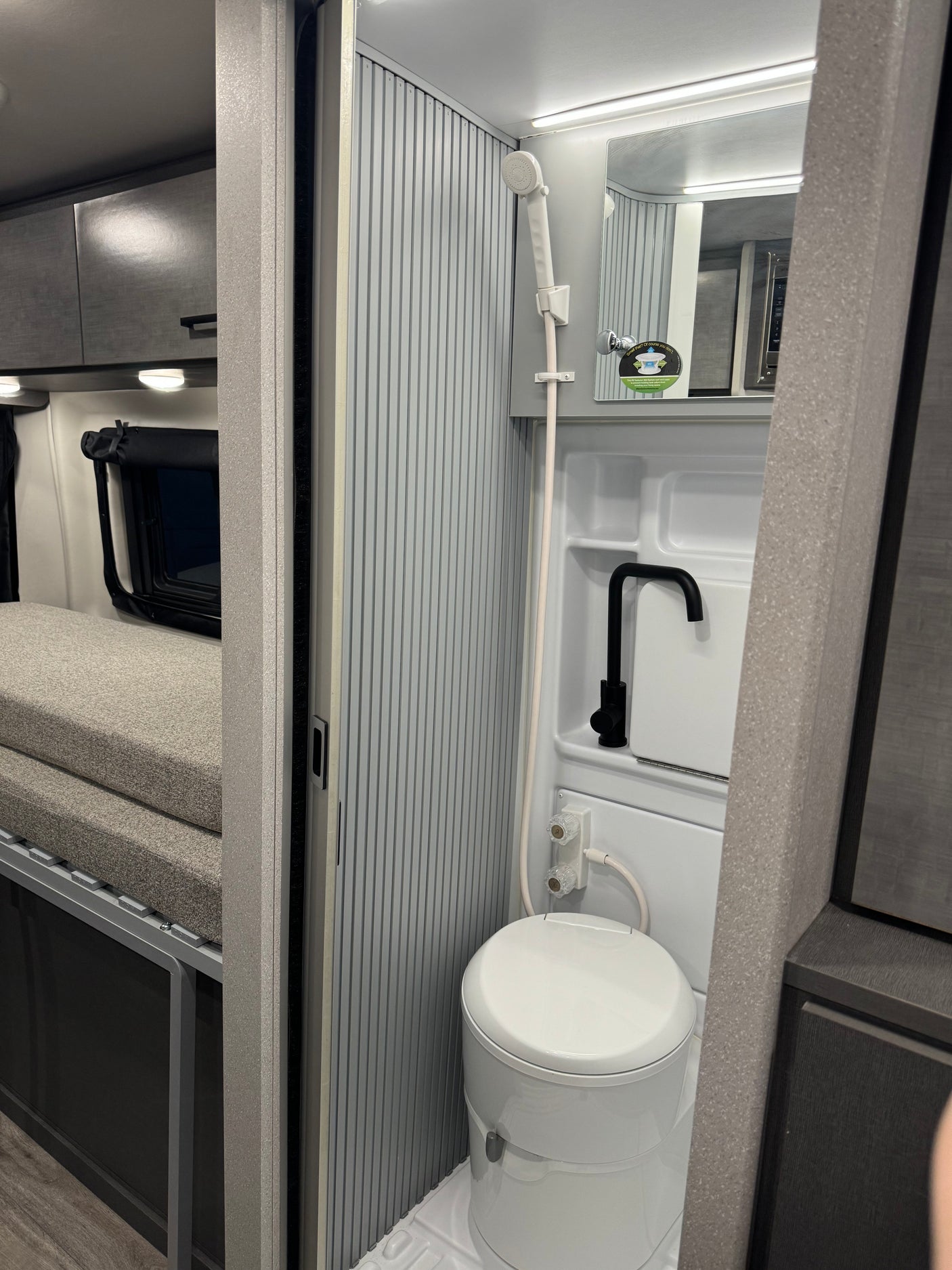 Compact RV rental interior shows a clever wet bath with shower, toilet, & sink, plus a comfy bed section. Great for travel.