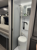 Compact RV rental interior shows a clever wet bath with shower, toilet, & sink, plus a comfy bed section. Great for travel.