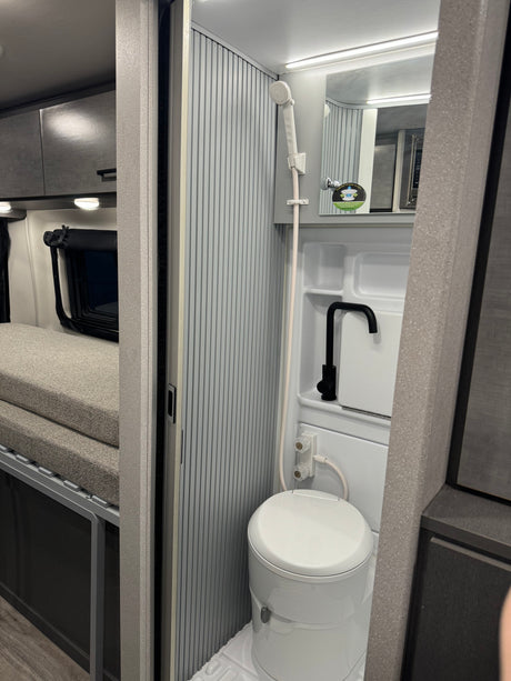 Compact RV rental interior shows a clever wet bath with shower, toilet, & sink, plus a comfy bed section. Great for travel.