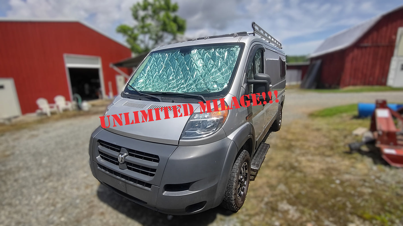 Unlimited mileage on this silver camper van for rv rental! Features a sunshade & roof rack, parked by red barns.