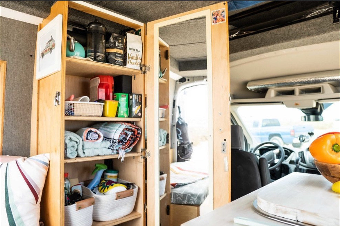Inside an organized RV rental: multi-shelf cabinets display kitchen, bath, & cleaning supplies. A compact counter holds fresh produce. — photo 9