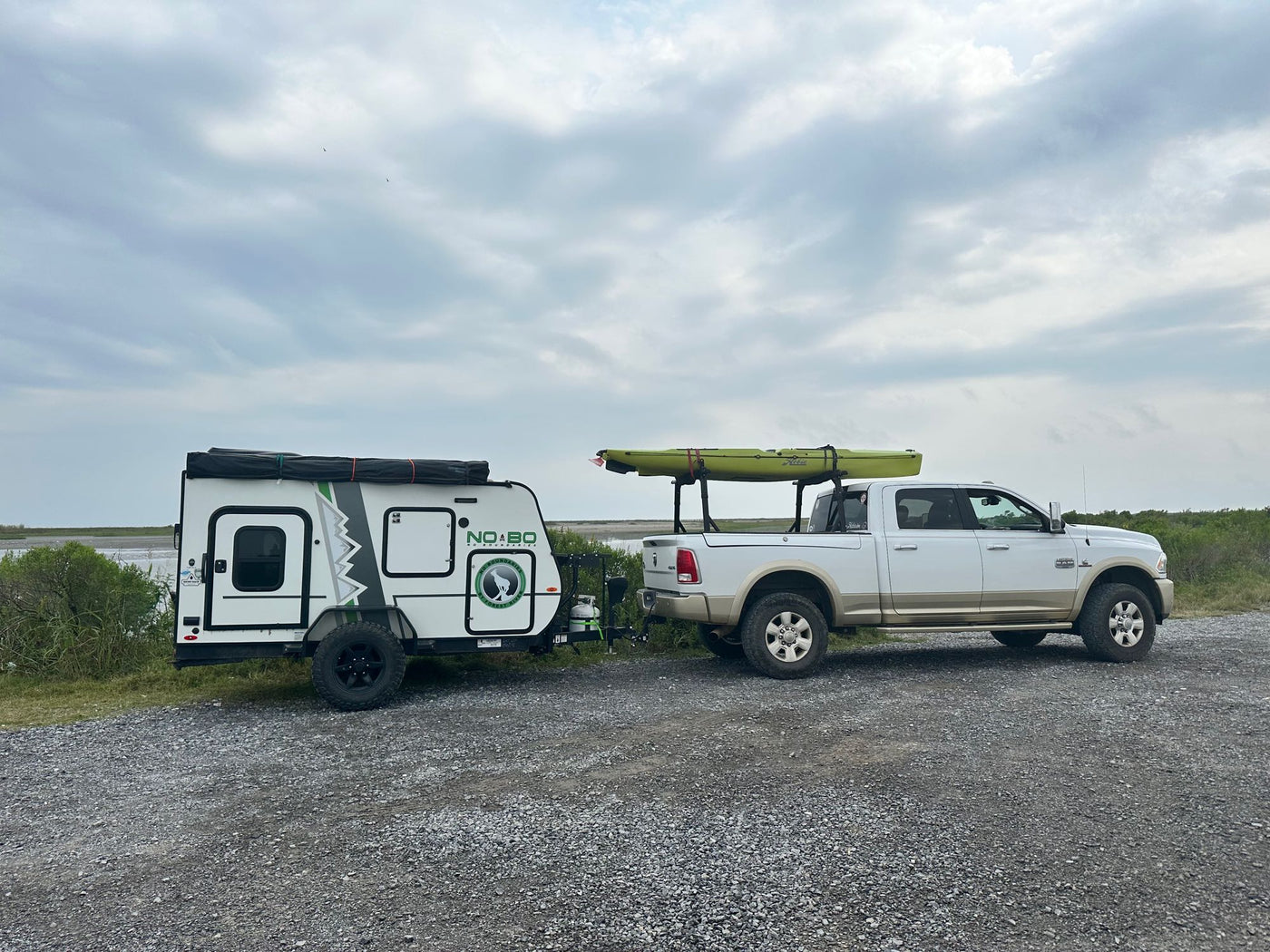 Truck with Hobie kayak towing a No Boundaries **RV rental** camper. Parked on gravel near water under cloudy sky, ready for adventure. — photo 14