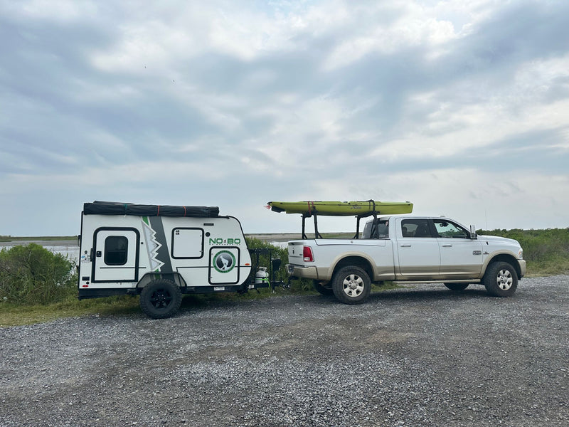Truck with Hobie kayak towing a No Boundaries **RV rental** camper. Parked on gravel near water under cloudy sky, ready for adventure. — photo 14