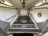 Inside a cozy pop-top RV rental, featuring a bed with a Grateful Dead blanket, window blinds, and an EXIT/SORTIE sign.