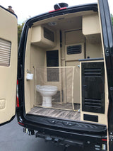 RV rental van's rear interior: compact toilet with mesh privacy screen, elegant cabinetry, and wood-look floor.