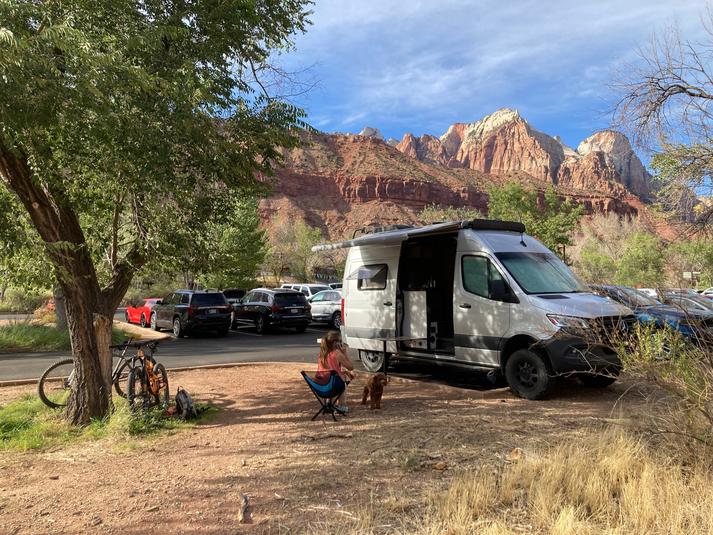 Enjoying an RV rental in Zion National Park, surrounded by majestic mountains. A woman, dog, & bikes near the van.