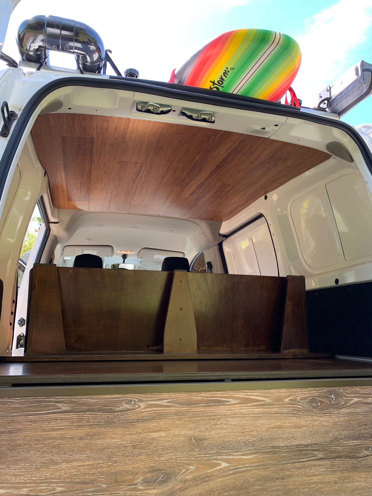 Explore this RV rental's custom interior: wood-paneled ceiling, partition, and a surfboard on the roof, ready for adventure.