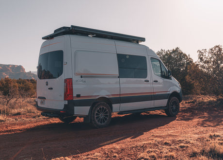 White Mercedes Sprinter camper van, ideal for rv rental adventures, parked on a dirt road with scenic red rocks.