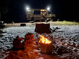 Cozy winter night camping with a bright fire, snow, and an RV rental. Perfect outdoor escape.