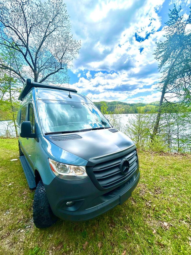 Explore nature! Modern blue Mercedes-Benz Sprinter van RV rental parked beside a lake, with trees and cloudy sky. — photo 4