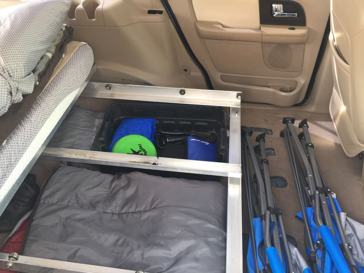 RV rental setup: vehicle interior with a custom storage platform holding a sleeping bag, gear, and folded camping chairs.