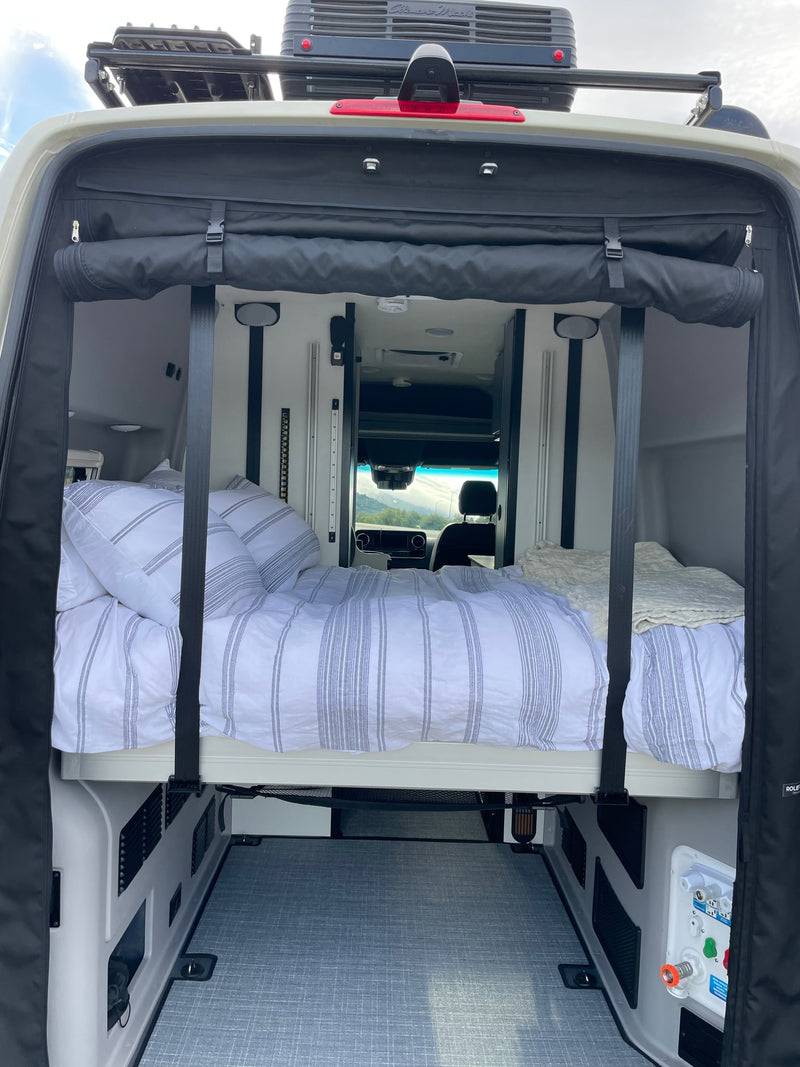 Inside an RV rental camper van: elevated bed with striped bedding, utility connections, and rear storage area, ideal for mobile living. — photo 5