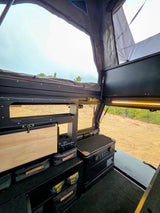 Interior of an overland RV rental camper with modular storage, a fridge, and a pop-top tent, ready for adventure.