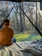 Young child gazes at sunlit forest from cozy RV rental bed, a serene nature retreat.