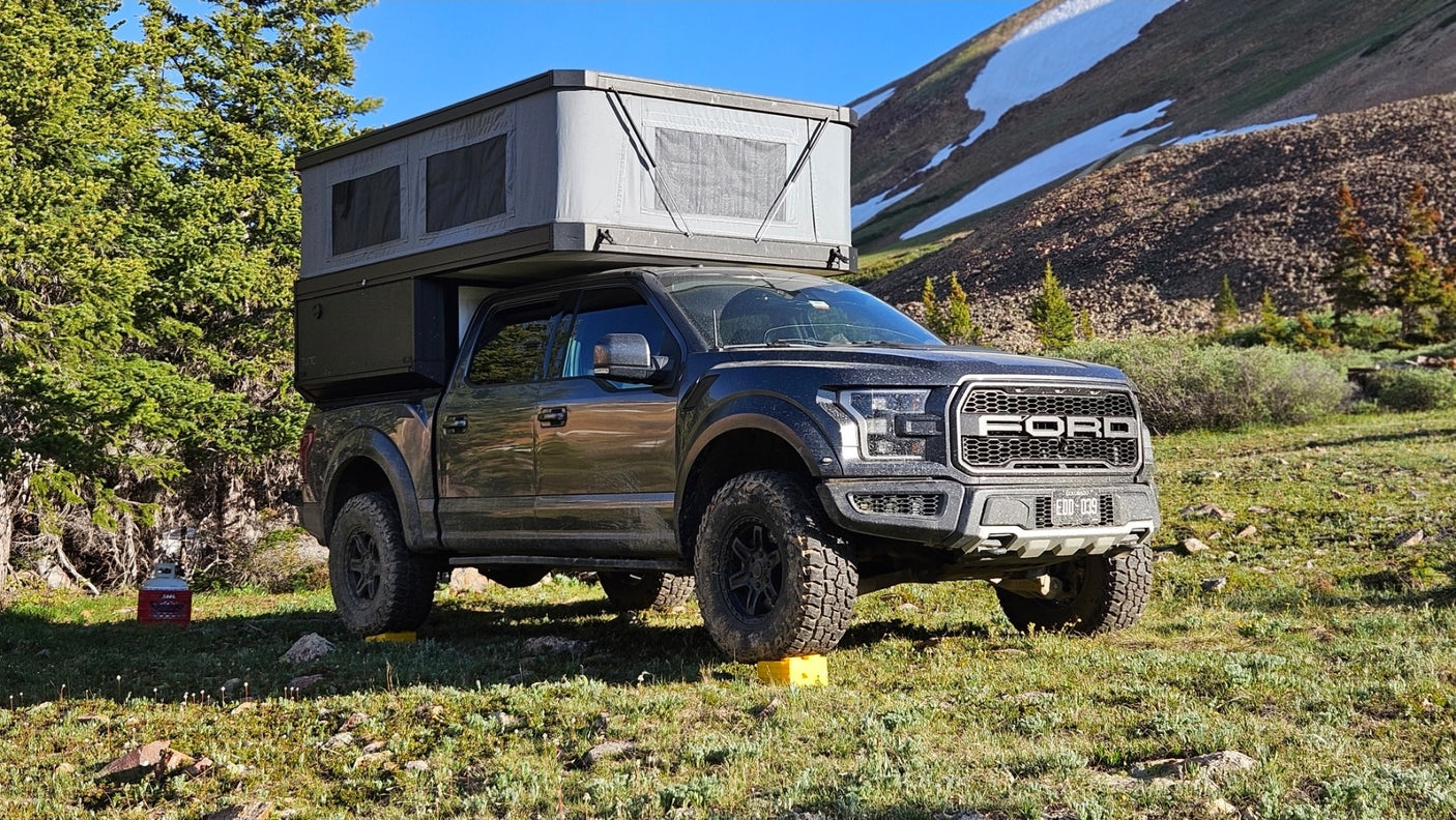 Off-road RV rental: a rugged Ford Raptor truck with a pop-up camper in a scenic mountain setting.