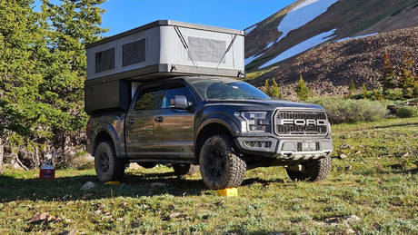 Off-road RV rental: a rugged Ford Raptor truck with a pop-up camper in a scenic mountain setting.
