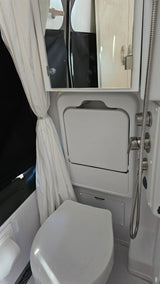 Compact RV rental bathroom with toilet, fold-down cover, showerhead, and mirrored cabinet, showcasing smart space utilization.