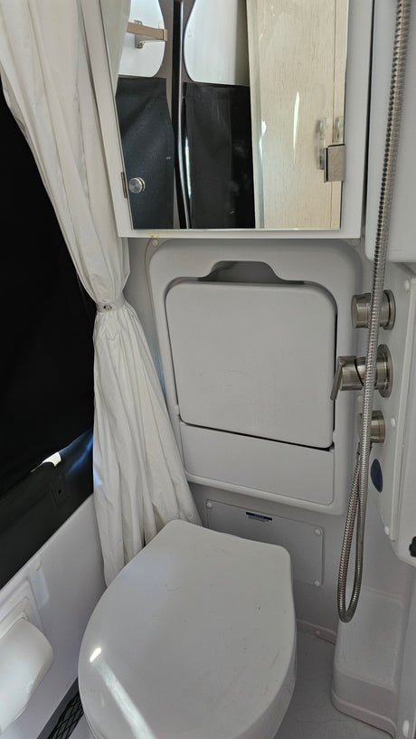 Compact RV rental bathroom with toilet, fold-down cover, showerhead, and mirrored cabinet, showcasing smart space utilization.