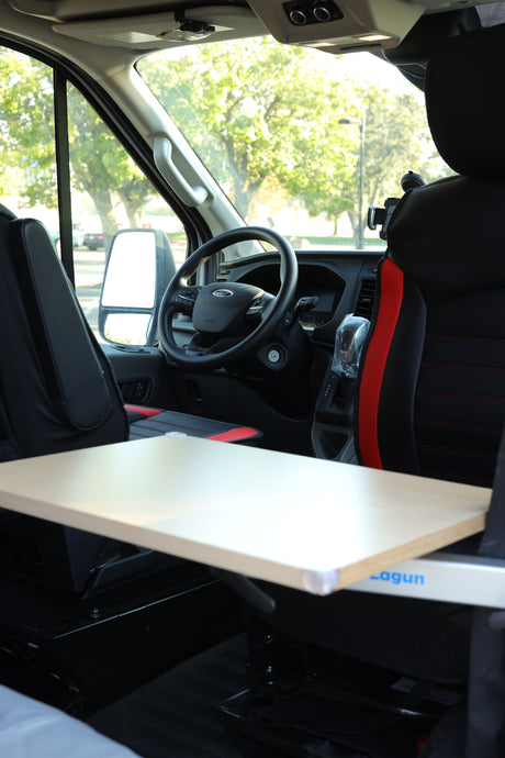 RV rental: Ford Transit interior with black seats, dashboard, and an adjustable Lagun table extending from the side.