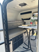 RV rental interior: A compact space with a grey dinette, bed area, table, and ceiling fan for comfortable travel.