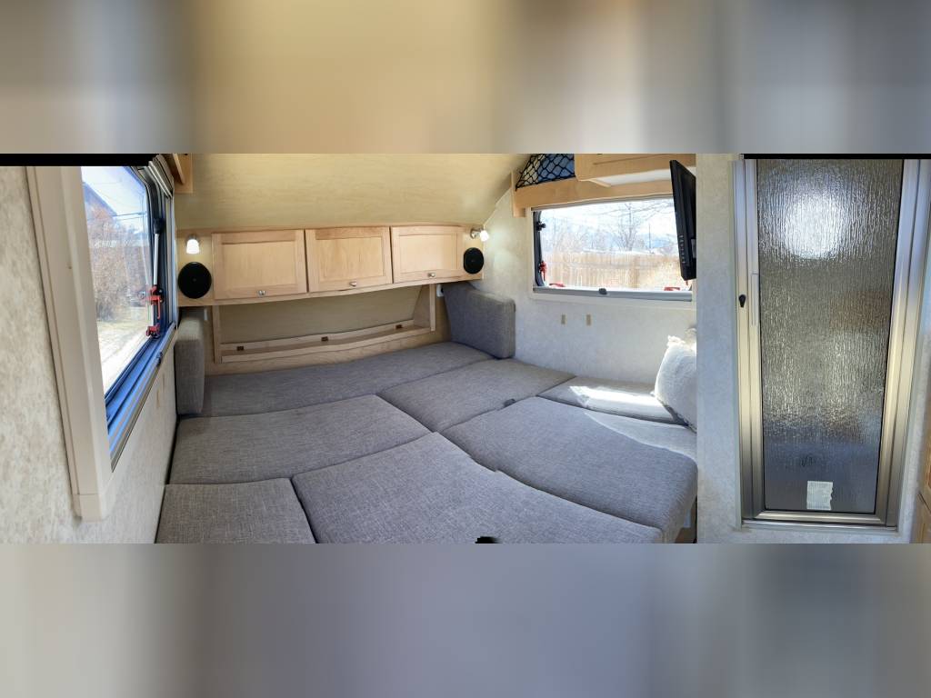 Cozy RV rental interior with a convertible bed, wood cabinetry, and large windows. Ideal for comfortable travel. — photo 6