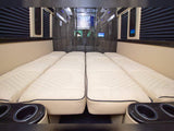Two rows of plush cream beds with quilted patterns and cup holders line this luxurious RV rental interior, ready for travel.