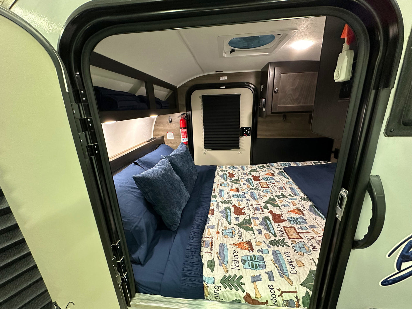 Cozy RV rental interior with a bed and camping-themed quilt, perfect for nature getaways.