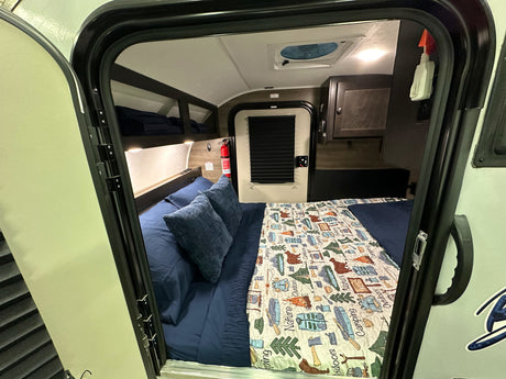 Cozy RV rental interior with a bed and camping-themed quilt, perfect for nature getaways.