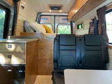Interior of a modern RV rental, featuring a bed, kitchenette, and passenger seats, ideal for travel adventures.