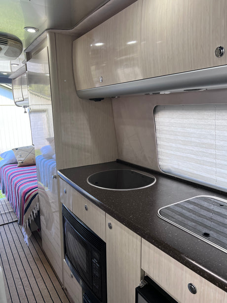 Step inside this RV rental! Modern interior with light wood cabinets, dark countertops, a built-in microwave, and a cozy bed.