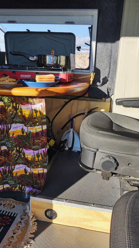 RV rental interior shows a compact kitchen with a red portable stove, bread, and a pot. A desert view is visible through the window.