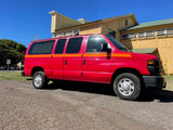 Bright red Ford E-Series passenger van, an ideal rv rental. Parked on a sunny day near a yellow building and green trees.