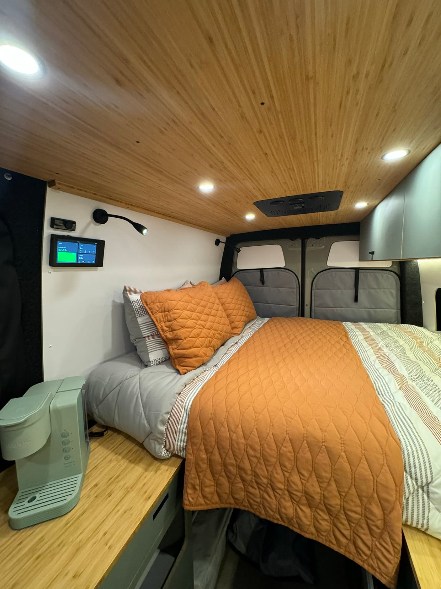 RV rental's cozy bedroom: comfy bed, wood ceiling, modern control panel, and coffee station for travel comfort.