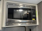 Modern stainless steel microwave oven, built into the cabinetry of an RV rental, glowing inside. Control panel on right.