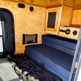 Cozy RV rental interior featuring light wood paneling, a dark blue bench/bed, integrated control panel, and a side door.