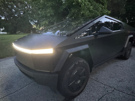 A sleek Tesla Cybertruck, front light on, parked. This electric truck offers unique trips; think beyond traditional RV rental.