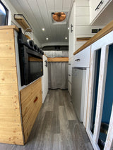 Inside an RV rental: a compact yet functional camper van kitchen with stove, refrigerator, and cozy sleeping area.