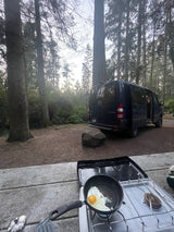 Enjoying an RV rental adventure: Frying an egg on a portable stove, with a camper van nestled in the forest.