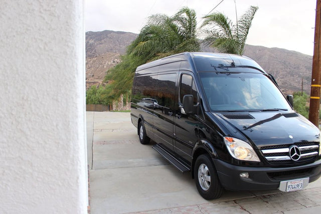 Black Mercedes-Benz Sprinter van, ideal for rv rental, parked on a driveway with mountains and palm trees behind it.